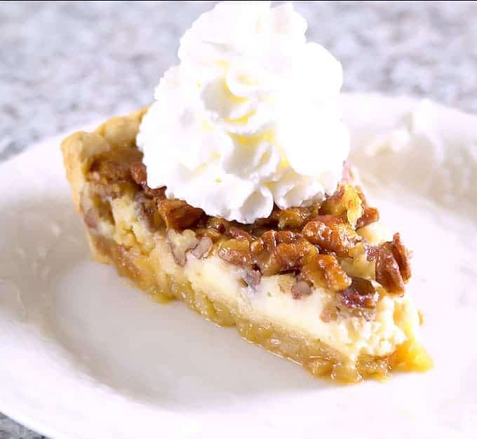 Cheesecake Stuffed Pecan Pie topped with whipped cream on a white plate