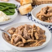 White bowl full of beef and noodles with green beans in the background.