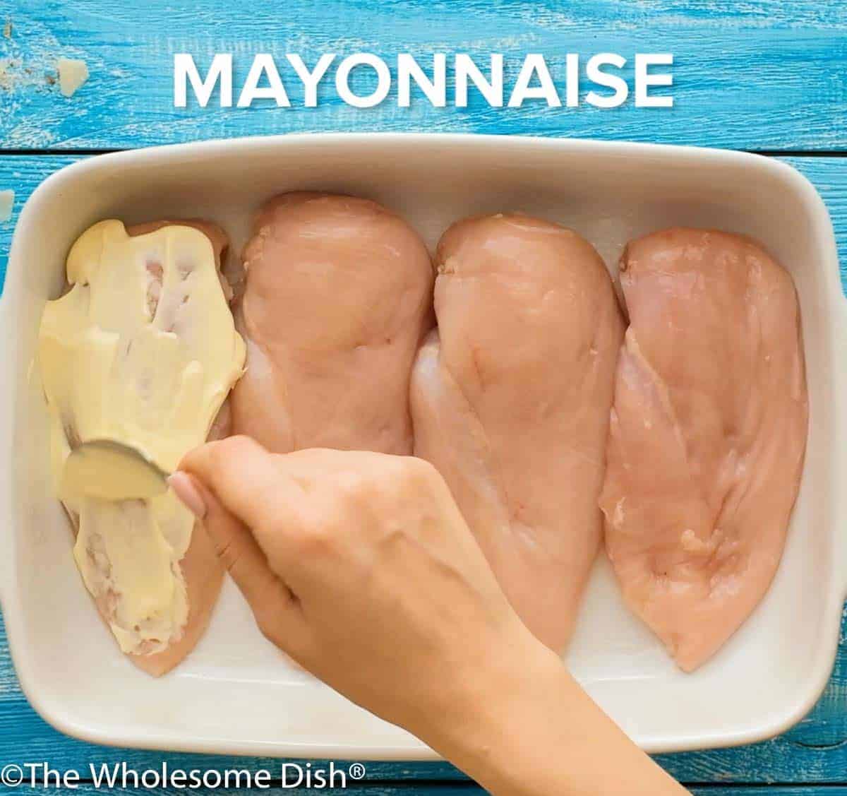 mayo being spread over uncooked chicken breasts in a baking dish