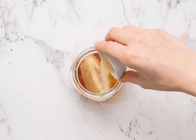 adding garlic powder to a mason jar with olive oil and red wine vinegar