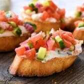 Greek Bruschetta Recipe with toast, creamy feta spread, and Greek seasoned toppings on a cutting board