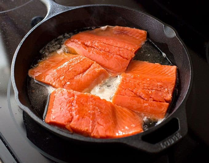 Salmon being cooked in a cast iron skillet