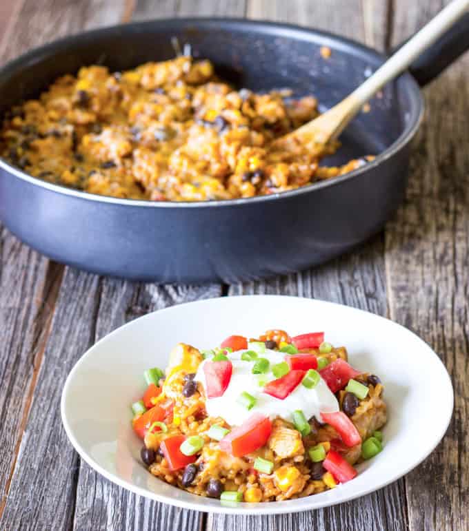 white bowl full of One Pot Wonder Chicken Enchilada Bowls with skillet in the background