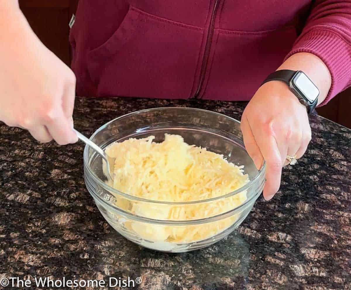 Three cheeses being mixed together in a glass bowl.