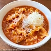 Lasagna soup topped with cheese in a white bowl.