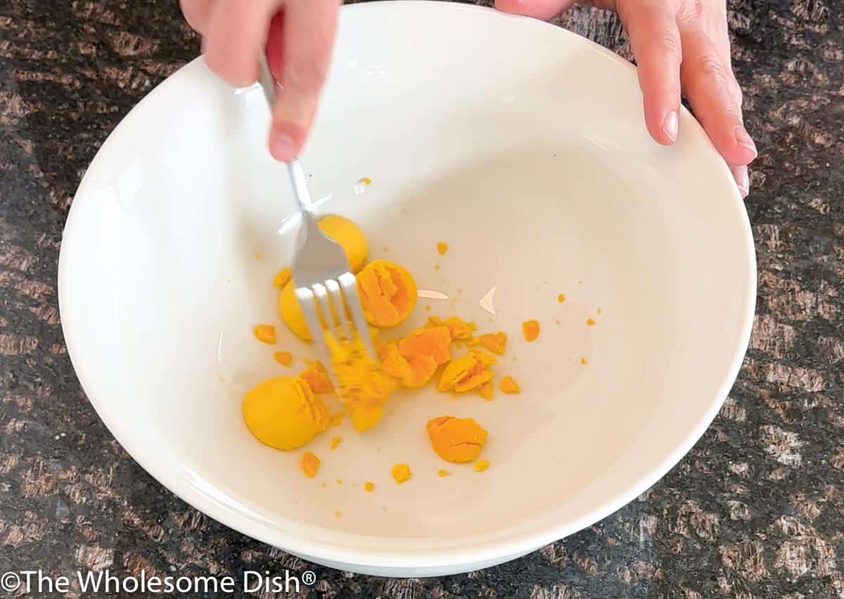 Egg yolks being mashed in a white bowl.