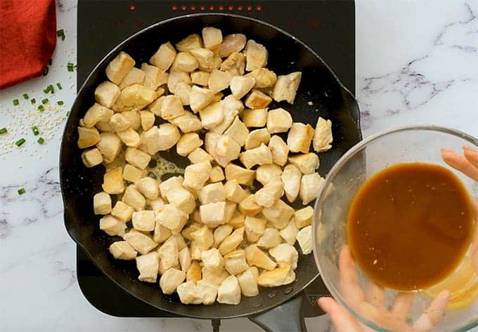 Skillet full of chunks of cooked chicken breast with mandarin orange sauce about to be poured over it.