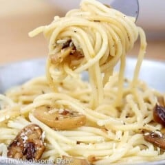 Fork full of mushroom pasta being lifted up out of a bowl.