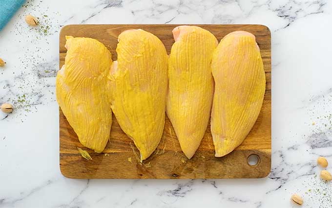 Four boneless skinless chicken breasts on a cutting board coated in honey mustard sauce