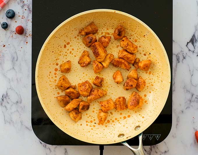 Chunks of chicken breast cooking in a skillet with olive oil and grill seasoning