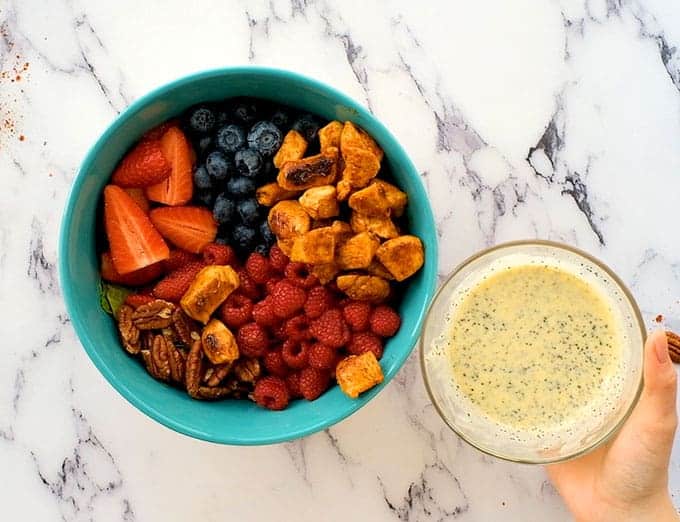 A bowl of seasoned chicken, pecans, strawberries, blueberries, raspberries, and lettuce with a small bowl of poppyseed dressing