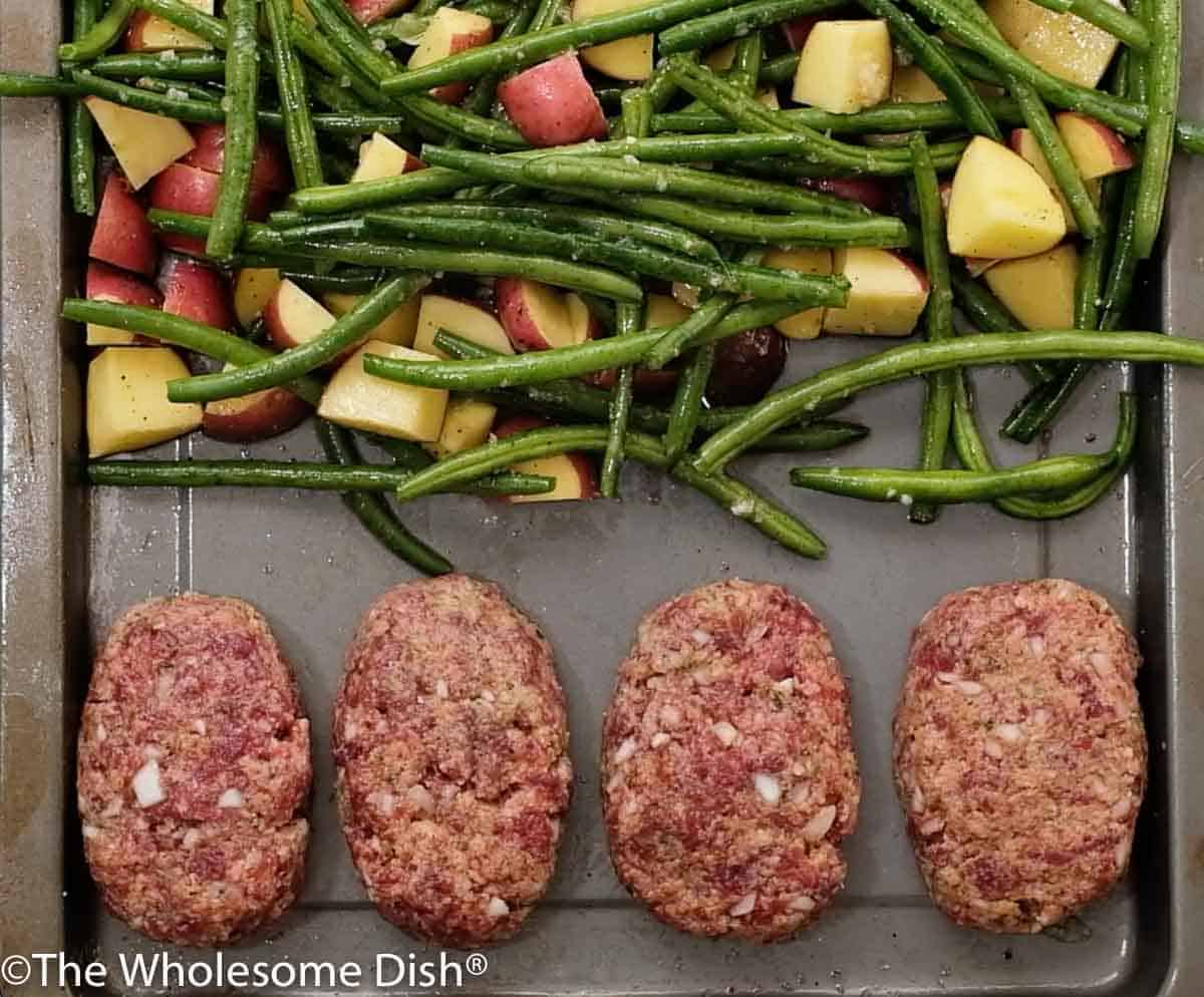 4 personal size meatloafs on a sheet pan with chopped potatoes and green beans ready to bake