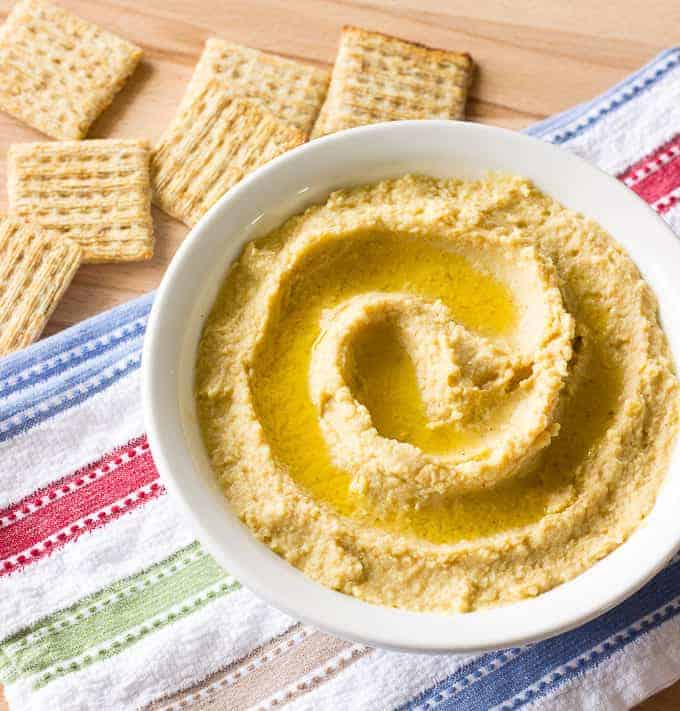 Simple Hummus Without Tahini in a white bowl with crackers on the side