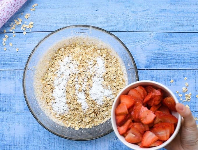 sliced fresh strawberries and oats going into a bowl for cheesecake baked oatmeal