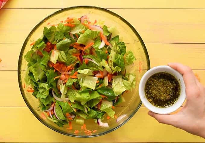 Lettuce, carrots, cheese, red onion, tomato, and Italian dressing in a large bowl for taco salad