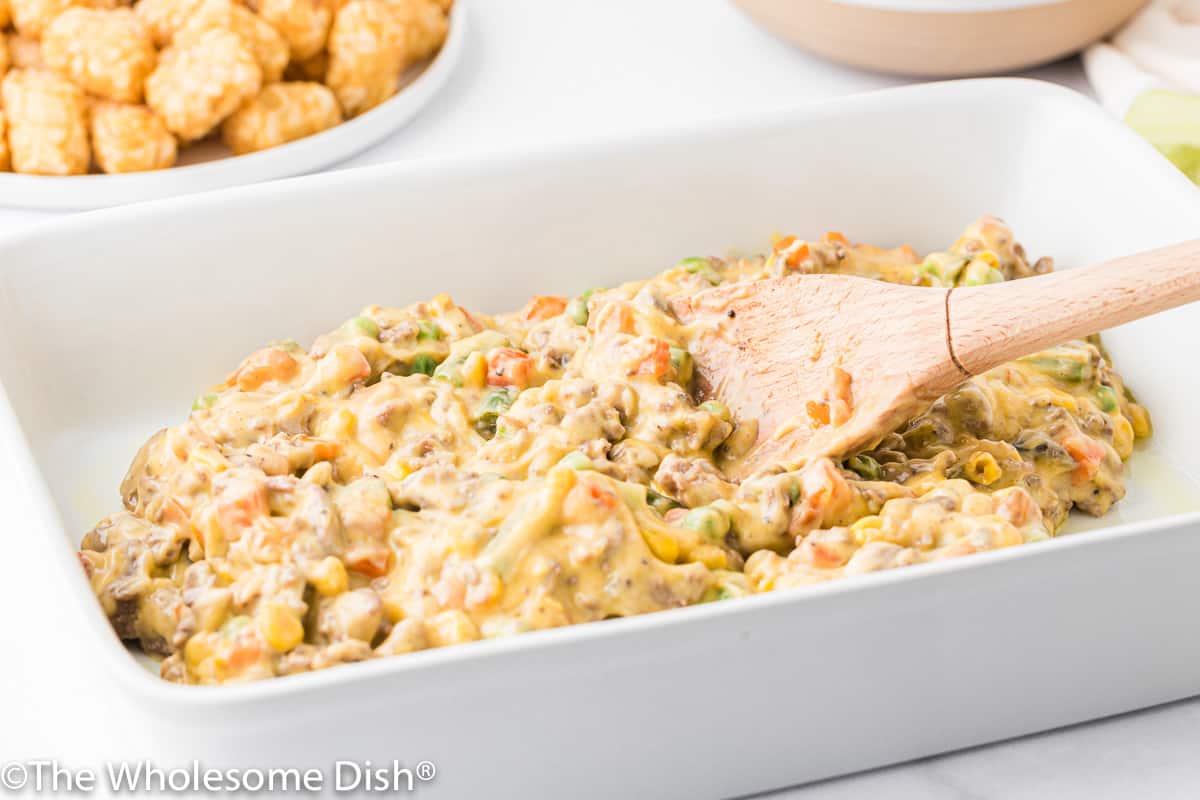 Tater tot hot dish filling being spread into a casserole dish.