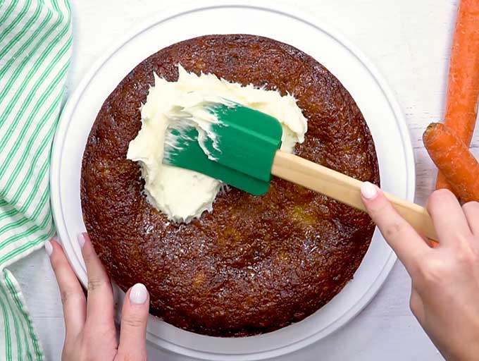 Spreading cream cheese icing on the best carrot cake recipe