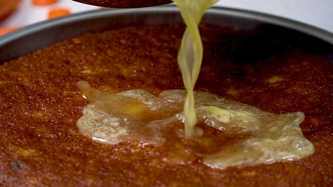 Pouring the sweet orange glaze over the warm carrot cake