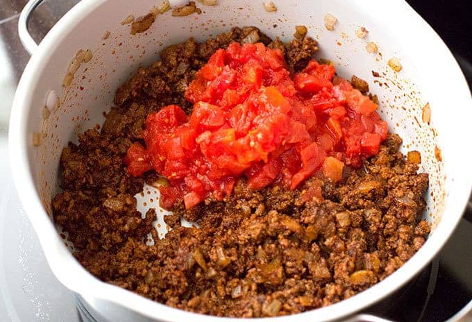 diced tomatoes over chili seasoned ground beef and onions in a soup pot