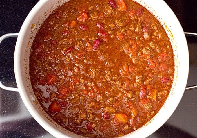 beans, beef broth, and tomato sauce added to chili seasoned beef, onions, and tomatoes in a pot