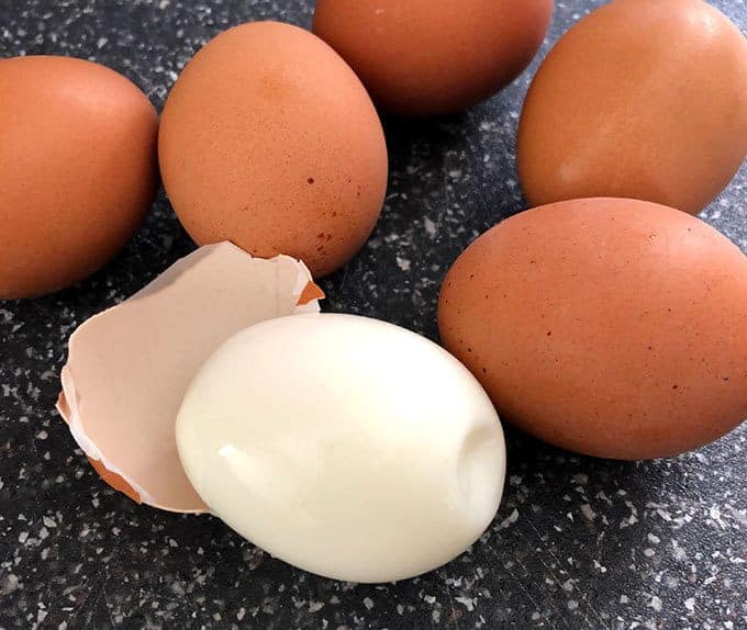 Hard boiled eggs on a cutting board. One egg has the shell removed.