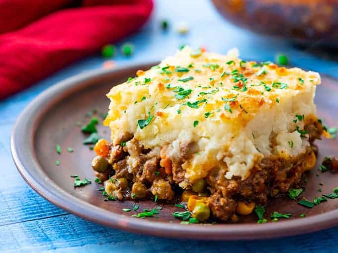 Piece of Shepards pie on a plate with layers of mashed potatoes and meat gravy with peas, carrots, onions, and corn