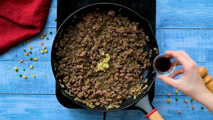 Adding minced garlic and worcestershire sauce to a skillet of ground lamb and chopped onions for The Best Classic Shepherd's Pie Recipe