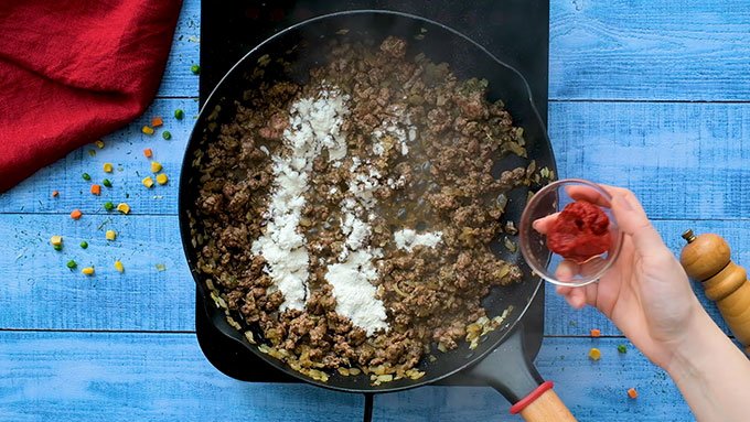 Adding flour and tomato paste to a skillet full of ground beef and onions for Easy Shepherd's Pie