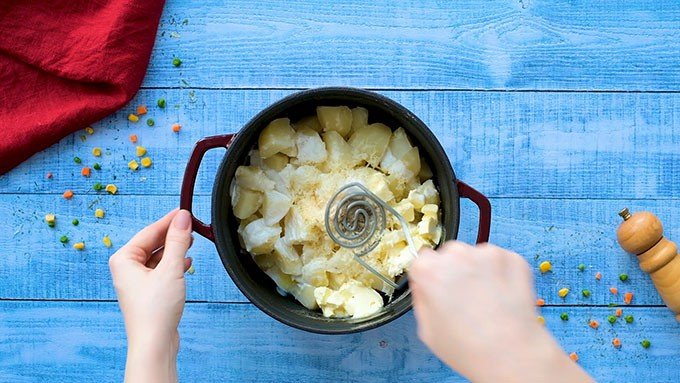 Mashing cooked potatoes in a pot with butter, half & half, parmesan cheese, garlic powder, salt, and pepper for Classic Shepherd's Pie