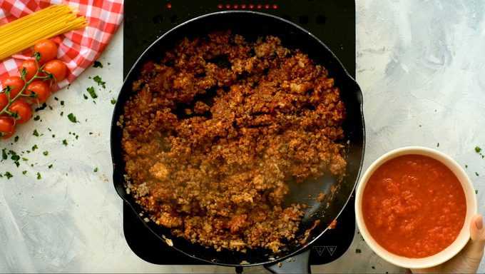 skillet full of cooked meat with tomato sauce about to be poured in.