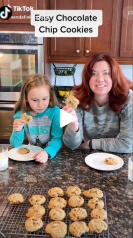 Mom and daughter in front of a counter full of chocolate chip cookies.