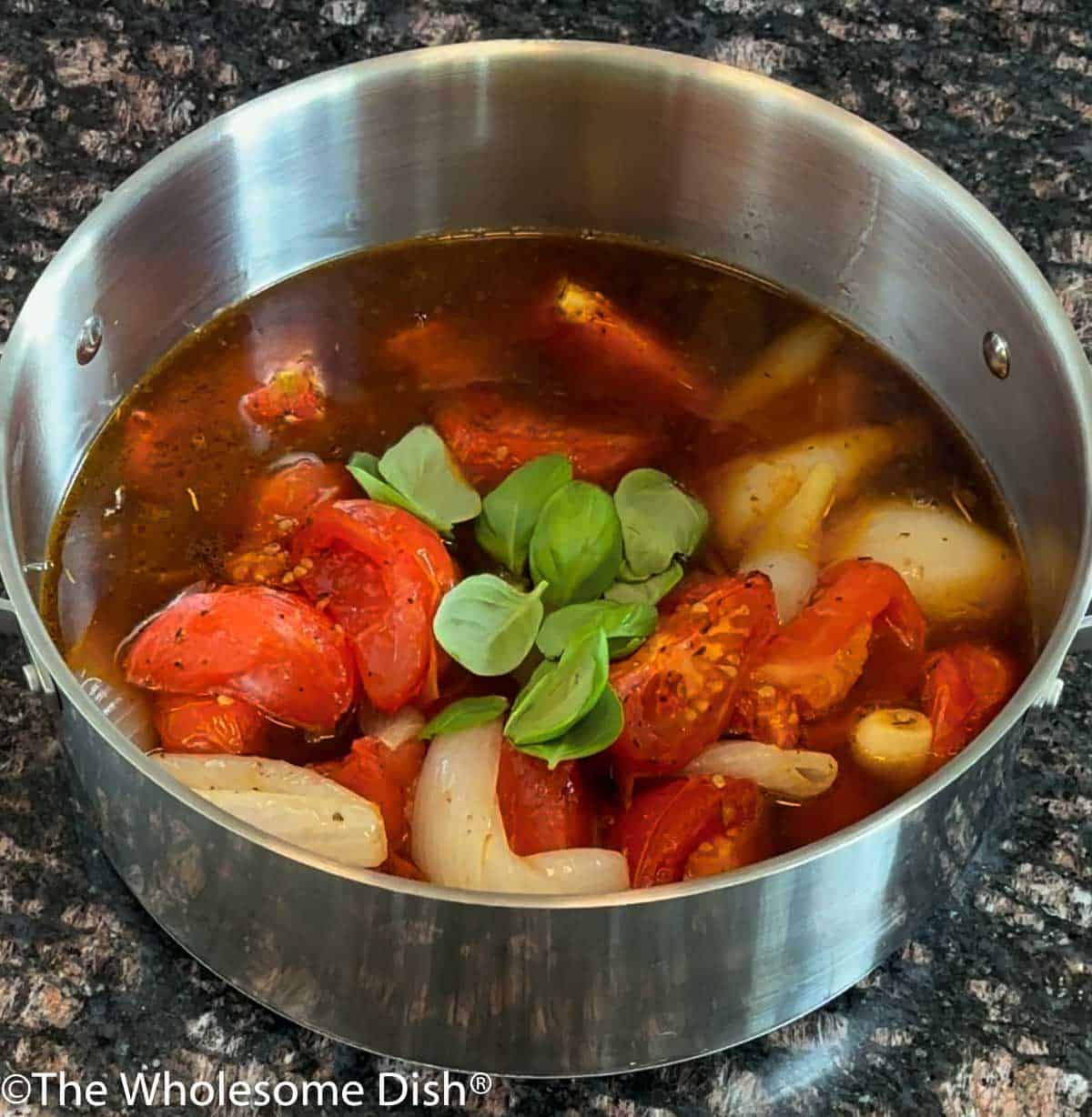 Adding broth and basil leaves to the roasted veggies.