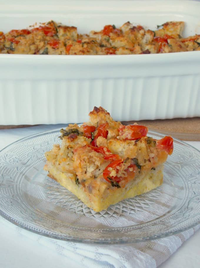 slice of tomato basil bread pudding on a plate with a baking dish in the background