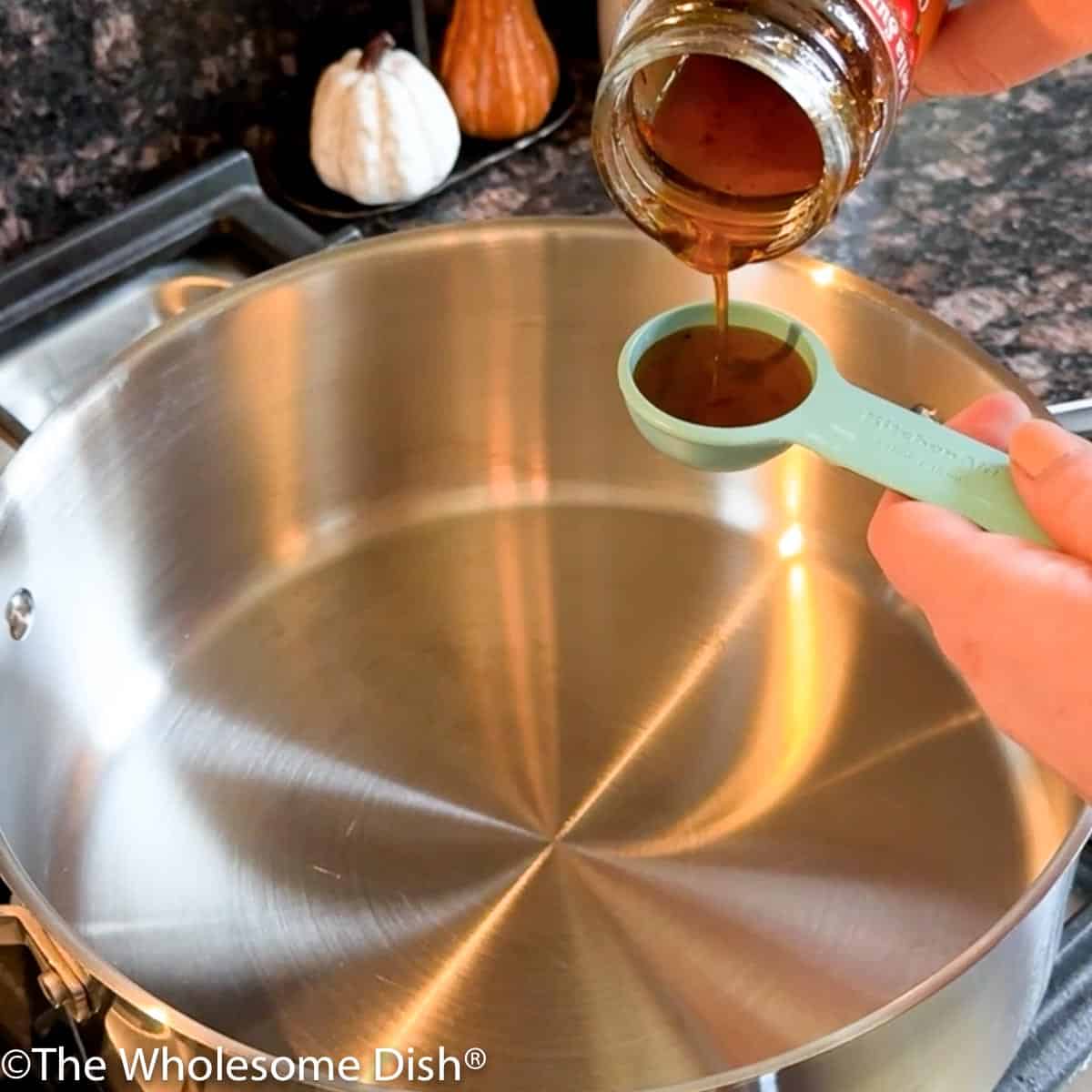 Pouring seasoned olive oil into a spoon over a soup pot.